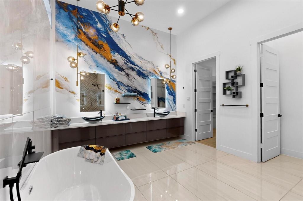 3946 North Cresthaven Road Dallas, TX 75209 - Photo 14 of 38 Bathroom featuring a freestanding soaking tub, dual floating vanities with vessel sinks, a statement wall with abstract art, and contemporary lighting fixtures