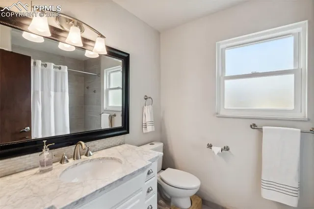 a bathroom with a granite countertop sink vanity mirror and toilet
