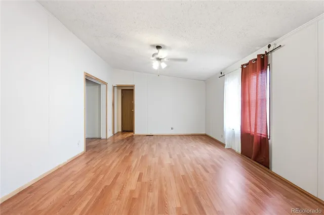an empty room with wooden floor chandelier fan and windows