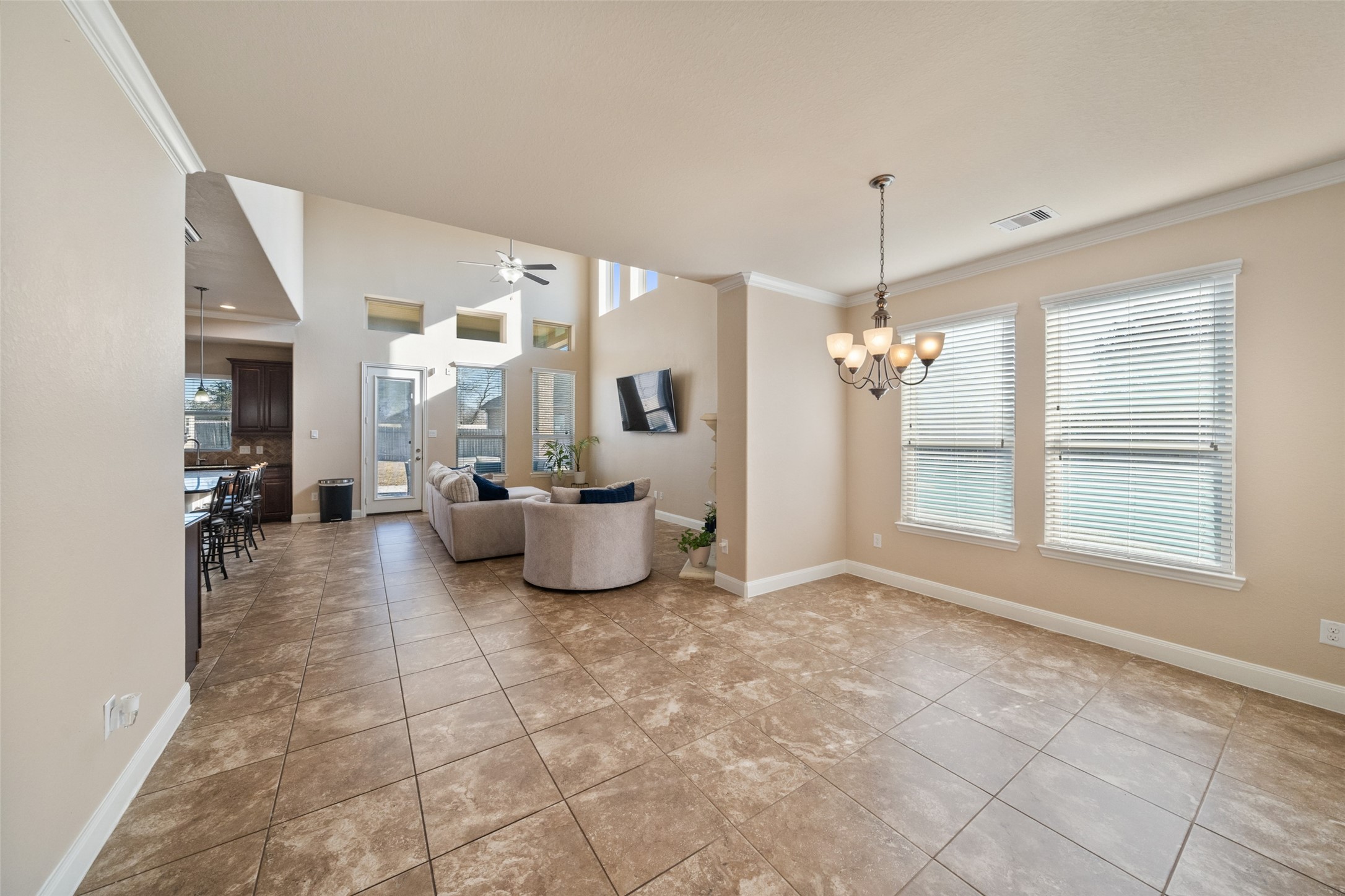 4747 Abercorn Street Rosharon, TX 77583 - Photo 8 of 46 This spacious, open-concept living area features tiled flooring, neutral walls, and abundant natural light from large windows. It includes a cozy seating area, ceiling fan, and a modern light fixture. The layout flows seamlessly into the kitchen and dining areas, with access to the outdoor space through a glass door.