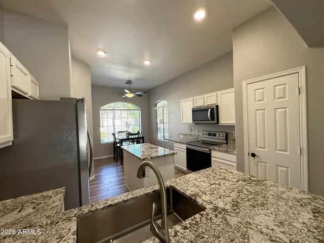 a kitchen with stainless steel appliances kitchen island granite countertop a refrigerator a stove top oven a sink dishwasher and dining table with wooden floor