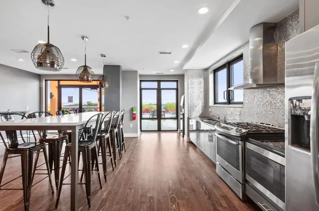 a kitchen with stainless steel appliances granite countertop a stove a refrigerator a kitchen island a dining table and chairs with wooden floor