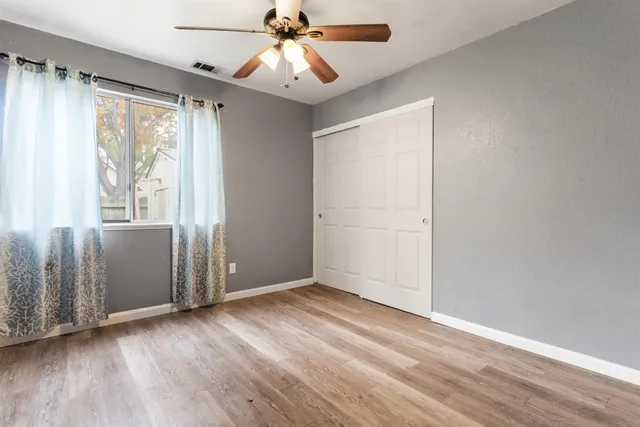 an empty room with wooden floor fan and windows