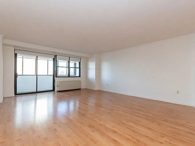 a view of an empty room with window and wooden floor