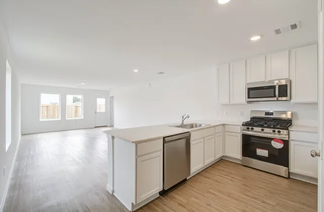 a kitchen with stainless steel appliances granite countertop a stove top oven a sink dishwasher and a refrigerator with wooden floor