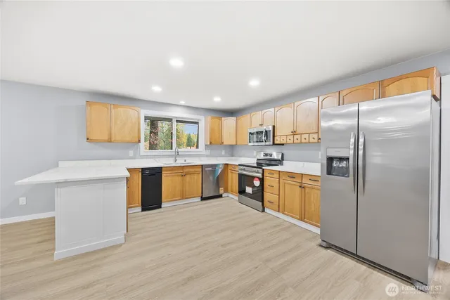 a large kitchen with a refrigerator a sink dishwasher a oven with white cabinets and wooden floor