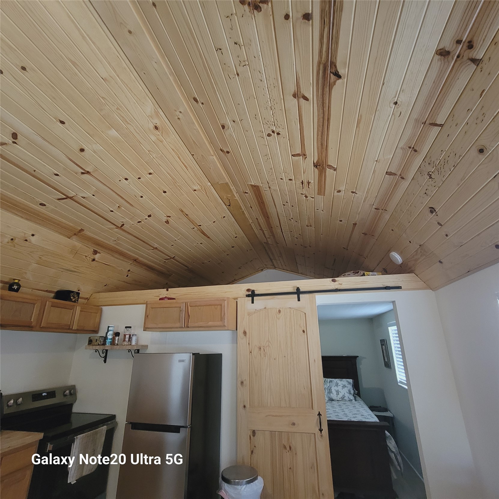115 Locust Road Stigler, OK 74462 - Photo 29 of 29 Vaulted wood-paneled ceiling, wood-finish cabinetry, stainless steel refrigerator, black range, and wood sliding barn door