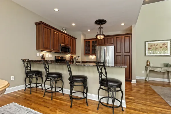 a kitchen with stainless steel appliances granite countertop a stove top oven a refrigerator a dining table and chairs with wooden floor