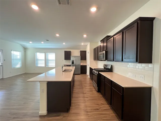 a large kitchen with stainless steel appliances kitchen island a sink dishwasher a stove and a refrigerator with wooden floor
