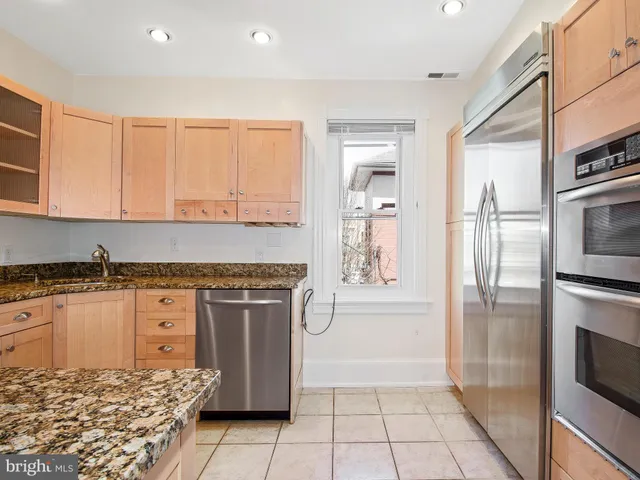 a kitchen with granite countertop a refrigerator oven a sink dishwasher and white cabinets with wooden floor