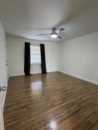 a view of an empty room with wooden floor and a ceiling fan