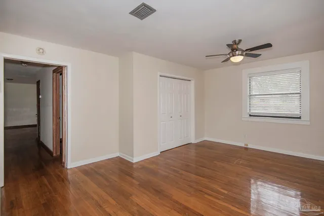 an empty room with wooden floor chandelier fan and windows