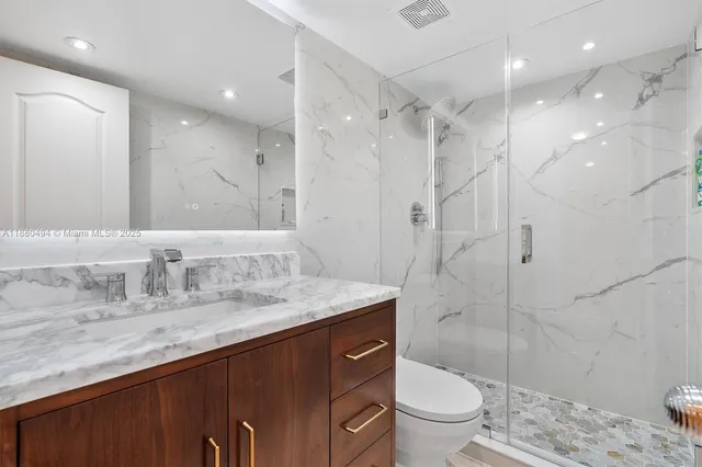 a bathroom with a granite countertop sink a toilet a mirror and shower