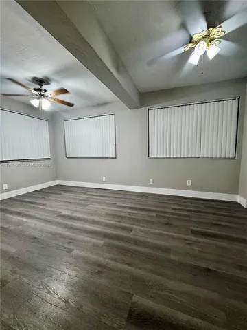 an empty room with wooden floor chandelier fan and windows