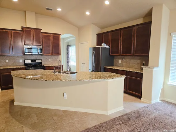 a kitchen with kitchen island granite countertop wooden cabinets a refrigerator and a sink