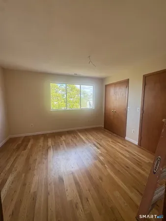 a view of an empty room with wooden floor and window
