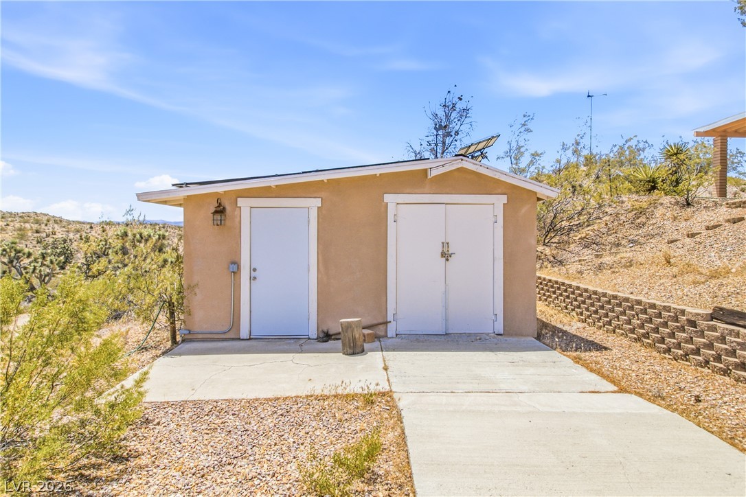 Rocking S Ranch Road Searchlight, NV 89046 - Photo 44 of 47 A detached storage structure with a concrete pad offers practical utility amidst desert landscaping.