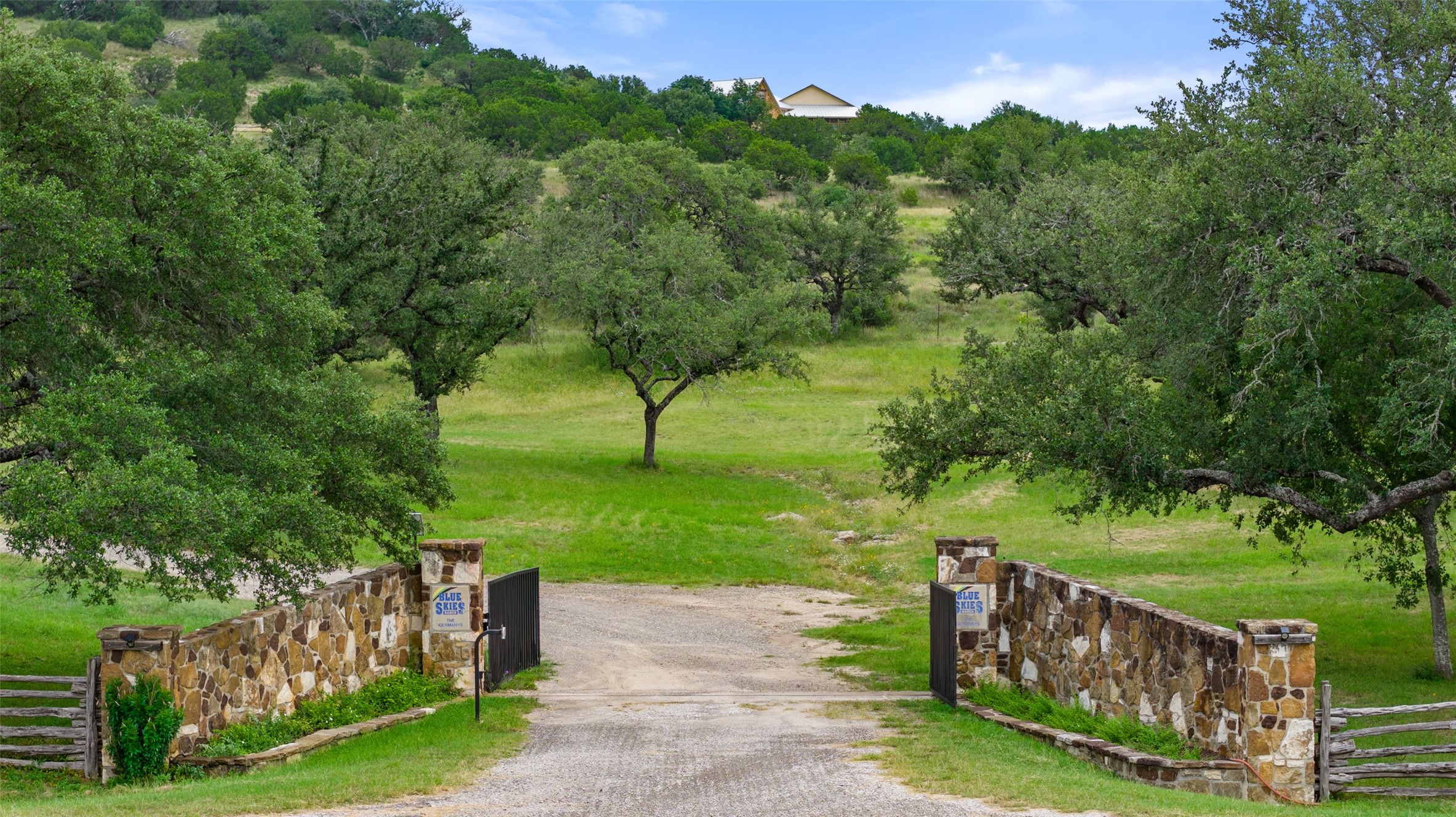 8400 Ranch Road 1431 Marble Falls, TX 78654 - Photo 23 of 30 A stone-walled entry gate welcomes you to an expansive, verdant landscape with mature trees and distant architecture.