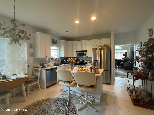 a room with stainless steel appliances kitchen island granite countertop a refrigerator a stove a sink dishwasher and a dining table with wooden floor