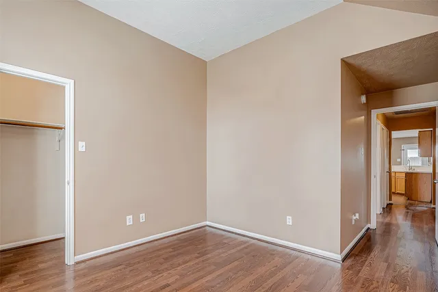 a view of an empty room with wooden floor and a bedroom