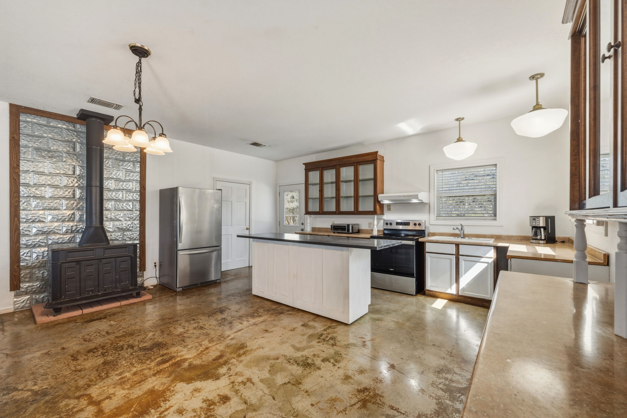 1301 Altwein Road Blanco, TX 78606 - Photo 13 of 40 Kitchen featuring concrete flooring, stainless steel appliances, a wood stove, glass fronted cabinets, and a center island