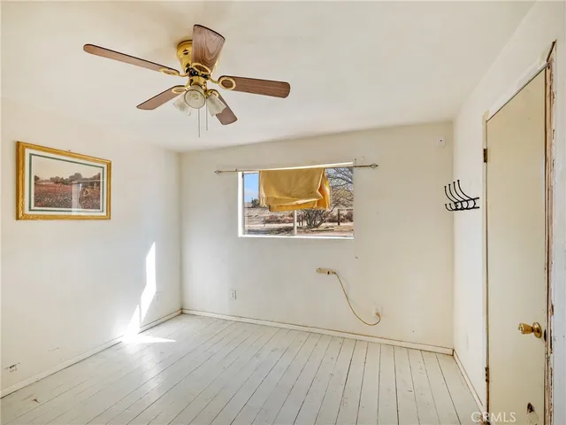 a view of an empty room with wooden floor and a ceiling fan