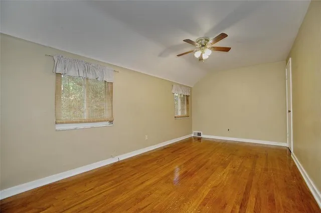 a view of an empty room with wooden floor and a fan