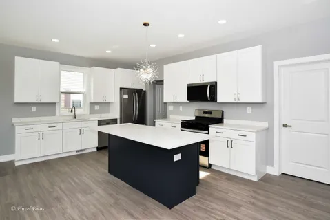 a kitchen with stainless steel appliances kitchen island granite countertop a stove top oven a sink a refrigerator and white cabinets with wooden floor