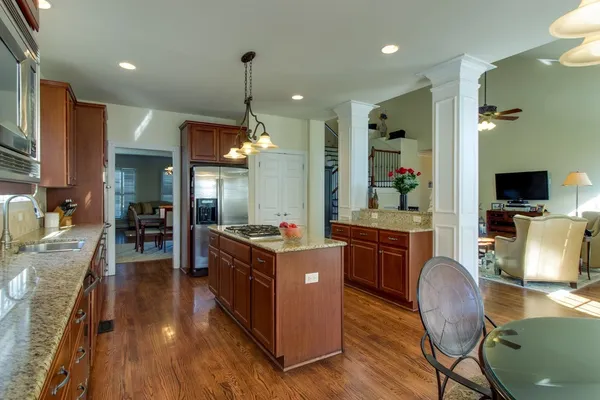 a kitchen with stainless steel appliances granite countertop a refrigerator a stove top oven a sink dishwasher a dining table and chairs with wooden floor