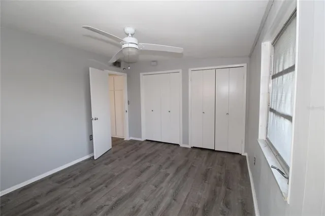 an empty room with wooden floor fan and windows