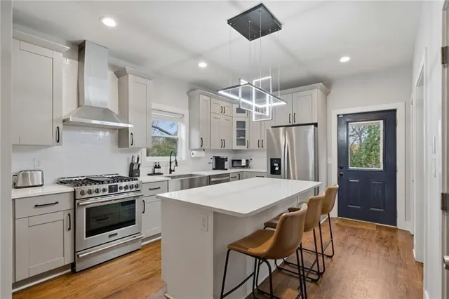 a kitchen with stainless steel appliances a stove a sink dishwasher a refrigerator with a dining table and chairs