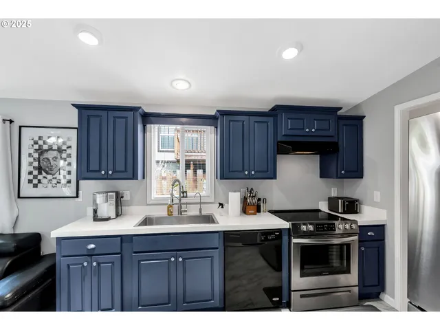 a kitchen with stainless steel appliances a sink a stove a refrigerator cabinets and a window