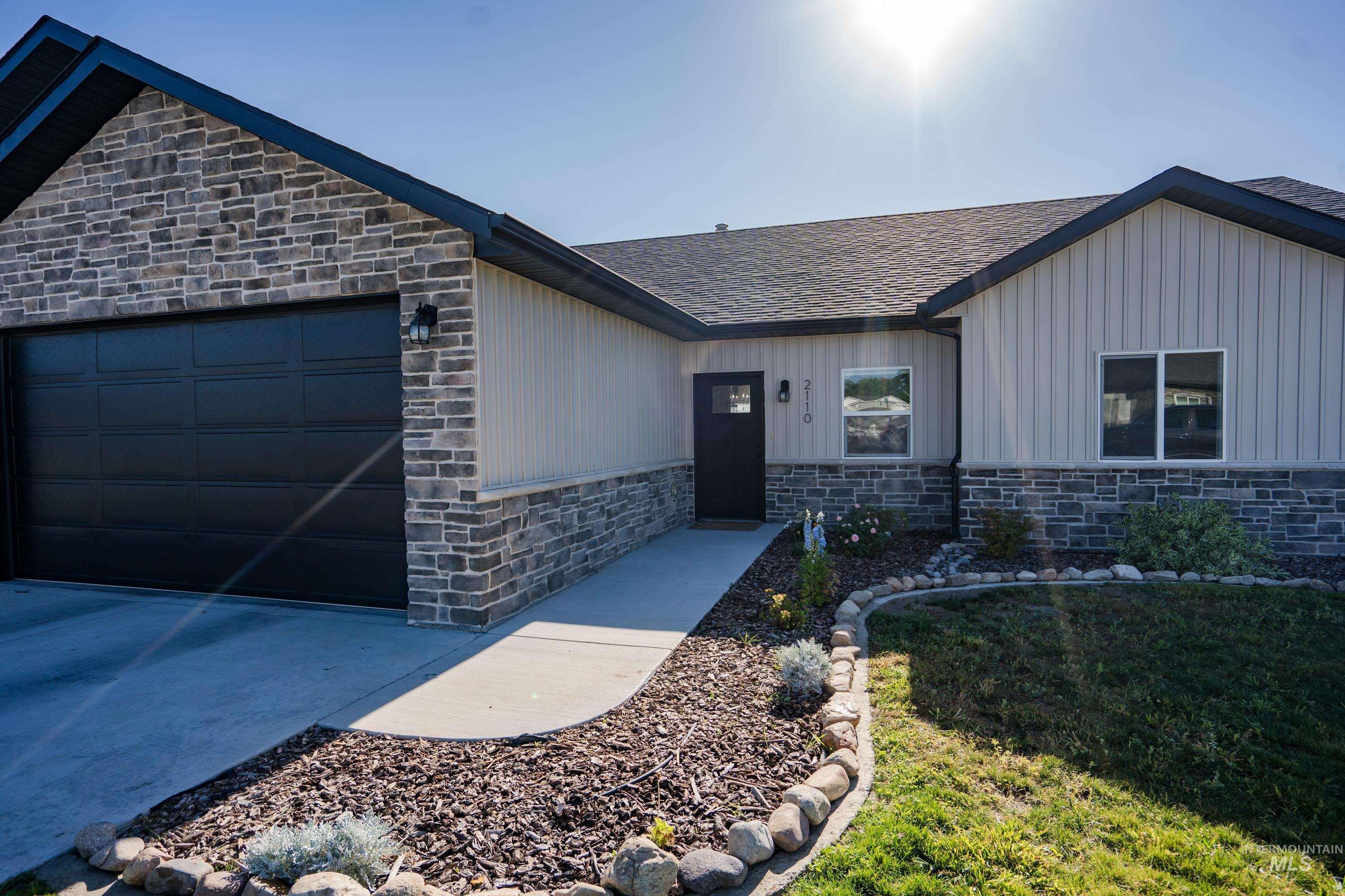 View of front of house with stone siding, an attached garage, roof with shingles, board and batten siding, and concrete driveway