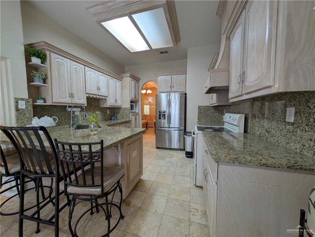 2000 East 25th Street Mission, TX 78574 - Photo 9 of 27 Kitchen with arched walkways, white range with electric cooktop, stainless steel fridge with ice dispenser, open shelves, and light stone counters