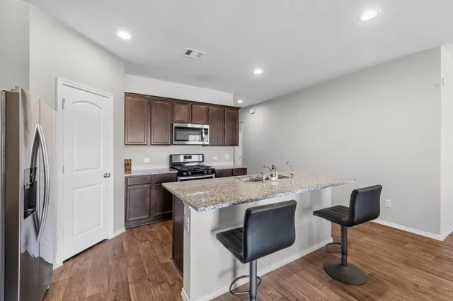 a kitchen with stainless steel appliances a stove top oven a refrigerator a sink and a refrigerator with wooden floor