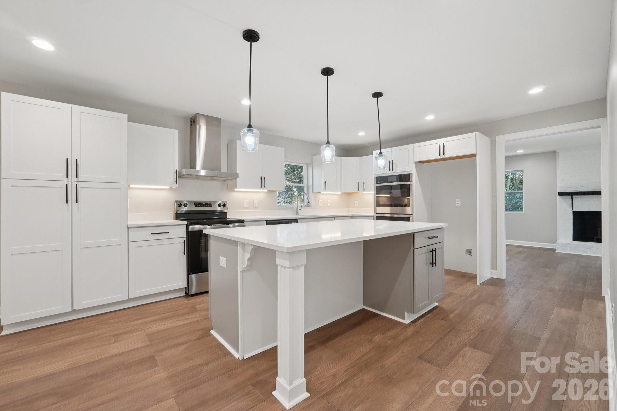 a kitchen with stainless steel appliances kitchen island a refrigerator a sink dishwasher a stove and white cabinets with wooden floor