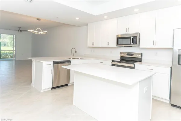 a kitchen with stainless steel appliances a sink a stove a microwave a refrigerator a white cabinets and wooden floor