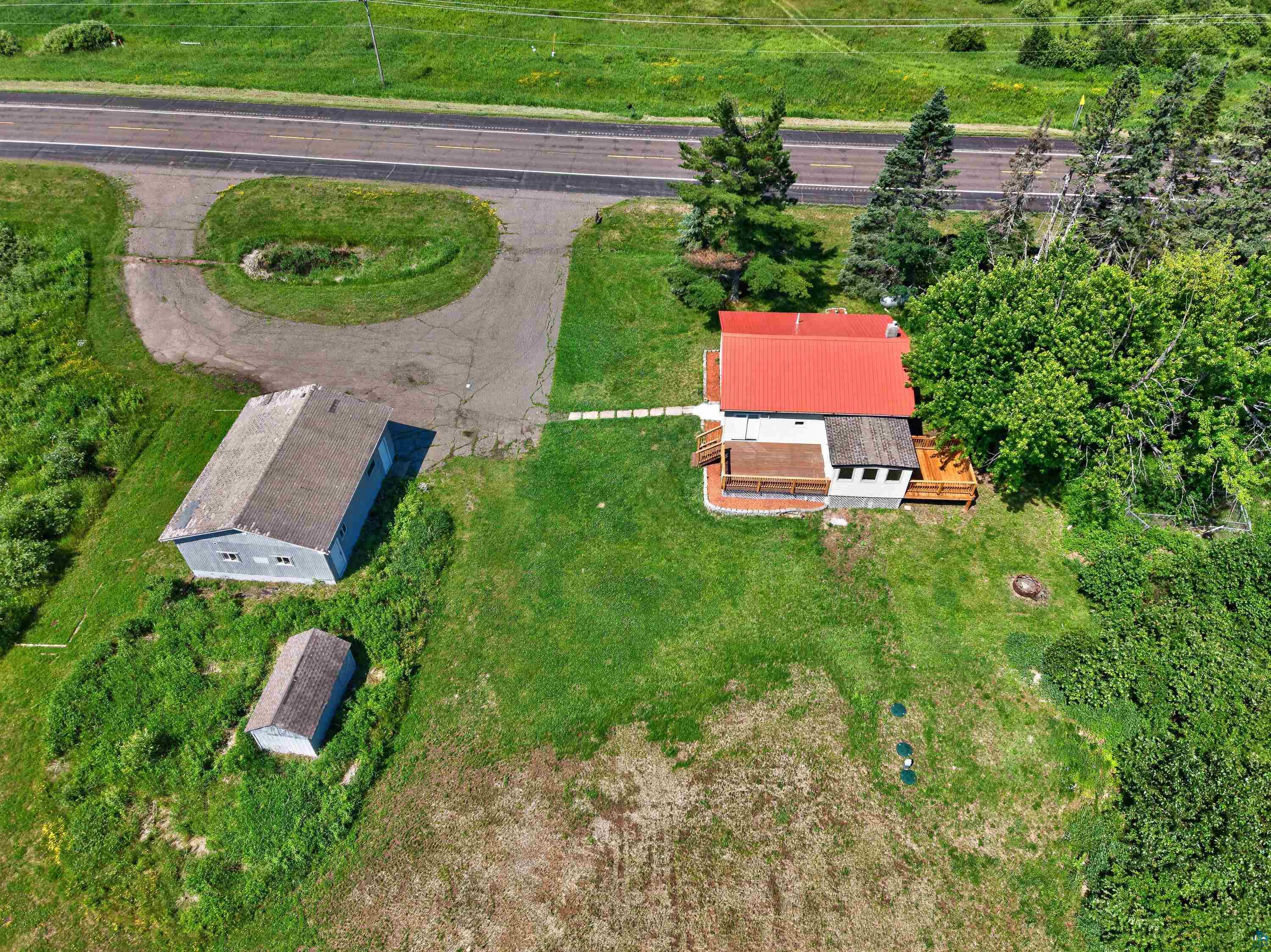 5868 Rice Lake Road Duluth, MN 55803 - Photo 9 of 39 Property featuring a main residence with a vibrant red roof, an expansive deck, and a detached two-story outbuilding with a gray roof