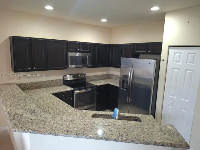 a kitchen with granite countertop wooden cabinets a refrigerator and a sink