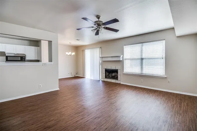 an empty room with wooden floor a ceiling fan a fireplace and windows