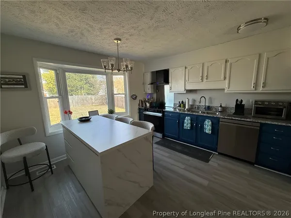 a kitchen with stainless steel appliances kitchen island granite countertop a sink dishwasher a stove top oven a dining table and chairs with wooden floor