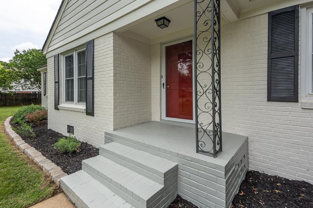 670 Peterson Lake Road Collierville, TN 38017 - Photo 2 of 37 Welcoming entryway featuring a red front door, painted brick facade, decorative wrought iron column, and a neatly mulched landscape bed with low-maintenance plantings