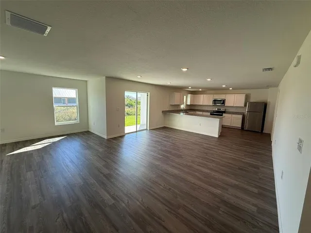 a view of a kitchen and an empty room with wooden floor and a kitchen