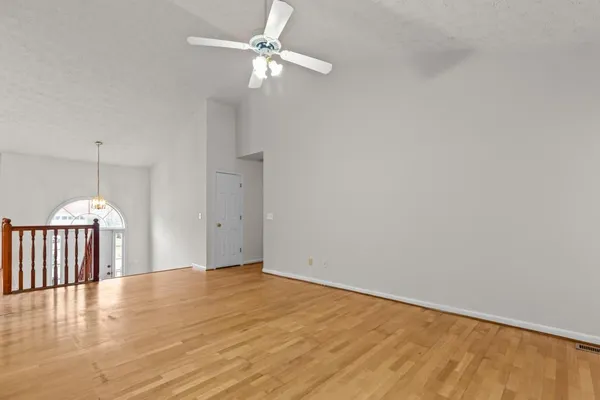 an empty room with wooden floor fan and windows