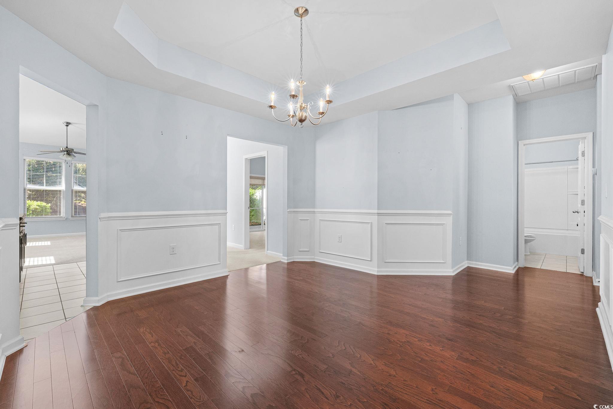 817 Arezzo Way, Unit 1001 Myrtle Beach, SC 29579 - Photo 9 of 40 Unfurnished dining area with a raised ceiling, wood finished floors, a decorative wall, a wainscoted wall, and a ceiling fan