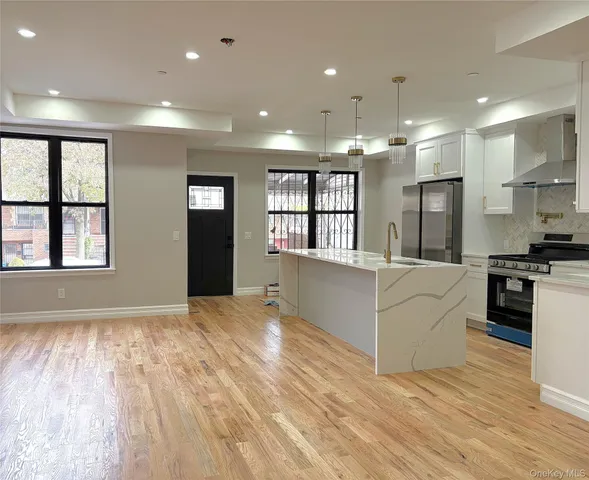a large white kitchen with kitchen island a sink wooden floor and a large window