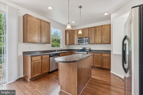 a kitchen with stainless steel appliances granite countertop a refrigerator a sink dishwasher a stove with wooden cabinets and floor