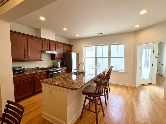 a kitchen with stainless steel appliances granite countertop a stove a refrigerator a sink a microwave and white cabinets with wooden floor