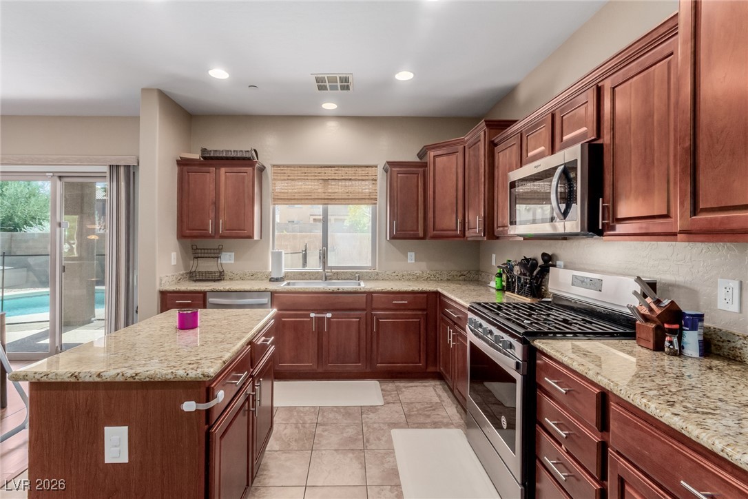 113 Lovage Street Henderson, NV 89002 - Photo 13 of 27 Kitchen featuring appliances with stainless steel finishes, light stone counters, light tile patterned flooring, a center island, and recessed lighting