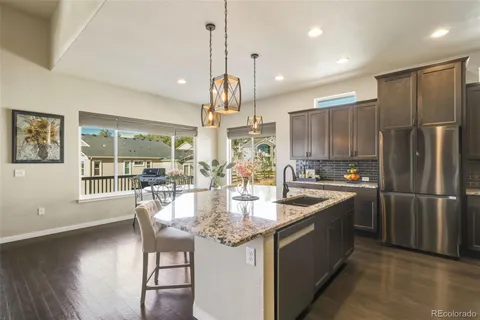 a kitchen with stainless steel appliances granite countertop a refrigerator a sink dishwasher a stove and a dining table with wooden floor